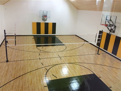 Indoor sports court with a wooden surface, featuring basketball hoops, black and yellow wall padding, and a volleyball net in the center in Woodland.