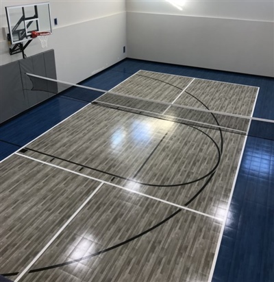 Indoor sports court with a gray and blue surface, featuring basketball hoops and a volleyball net in the center.