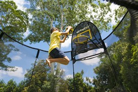 Black trampoline with a black safety net, a child jumping on it, and a basketball hoop in Elm Grove.