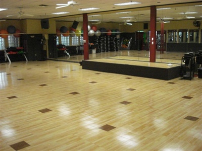 Multipurpose exercise room with wooden floors, small squares with dark wood, and a raised platform. 