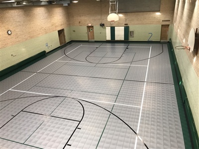 An indoor basketball court with a grey and green surface and black and white lines.