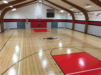  An indoor basketball court with a polished wood surface, red key areas, and a central logo, enclosed by arched wooden beams in Madison.