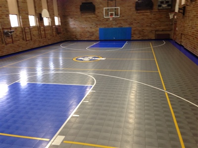 An indoor basketball court with a grey and blue surface, yellow lines, and a central logo, set against brick walls in Milwaukee.