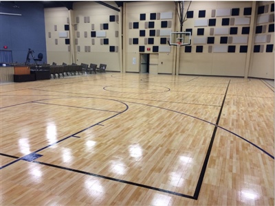 An indoor basketball court with a polished wood surface, black lines, and a modern wall design featuring square patterns.