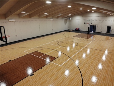 An indoor basketball court with a polished wood surface, brown key areas, and black lines, enclosed by an arched ceiling with bright lighting Lake Geneva.