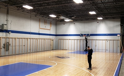 An indoor basketball court with a polished wood surface, blue key areas, black lines, and featuring a central logo in Elm Grove.