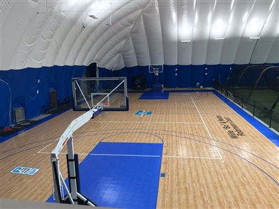 An indoor basketball court with a polished wood surface, blue key areas, and black lines, featuring a white arched ceiling and blue walls in Fox Point.