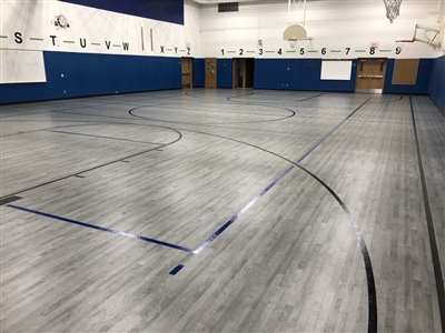  An indoor basketball court with a grey wood-like surface, black and blue lines, and blue walls, featuring multiple basketball hoops in Shorewood.