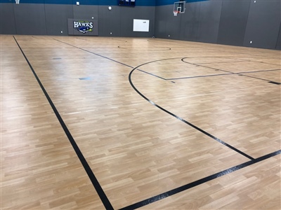 An indoor basketball court with a light wood surface, black lines, and grey walls in Madison.