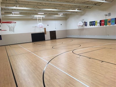 An indoor basketball court with a light wood surface, black lines, and white walls, featuring multiple basketball hoop.