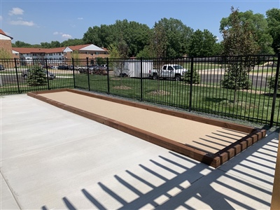 Outdoor bocce ball court with wooden borders, located next to a concrete walkway and fenced area.