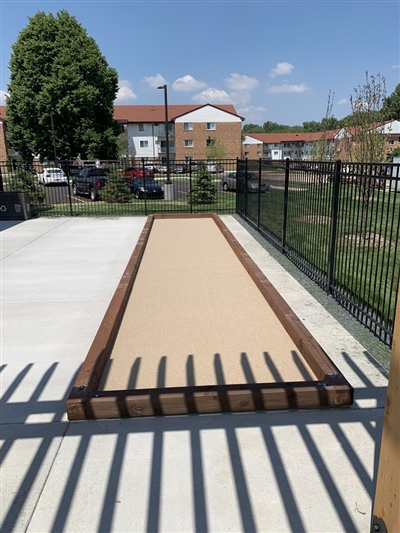 Outdoor bocce ball court with wooden borders, located next to a concrete walkway and fenced area in Wasuau.