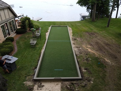 Outdoor bocce ball court with green turf and low border wall.