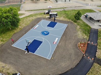  Outdoor sports court with a gray and blue surface, featuring two basketball hoops and the Minnesota Timberwolves central logo.