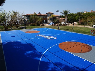  Outdoor residential basketball court with a blue surface, large orange basketball designs, and a white logo in Eau Claire.