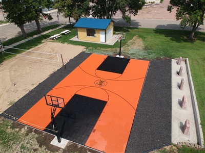 Outdoor residential basketball court with an orange and black surface, featuring two basketball hoops.