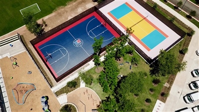 Outdoor sports complex with two courts: one blue and red basketball court with white lines, and one yellow and teal court in Green Bay.