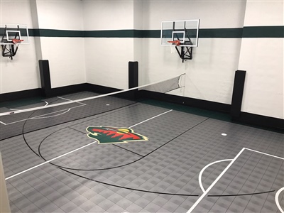 A small indoor basketball court with a grey surface, black lines, and white walls, featuring a Minnesota Wild central logo and two basketball hoops.