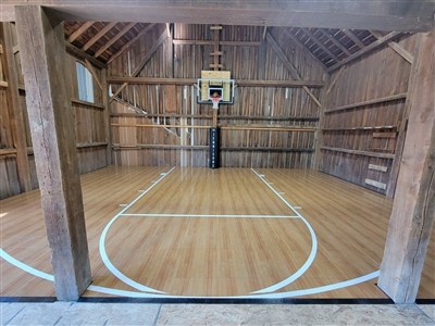 A small indoor basketball court with a polished wood surface, white lines, and rustic wooden walls.