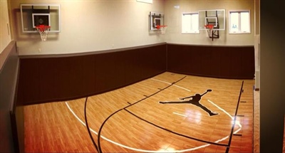 Indoor home basketball court with polished wood flooring, a central Jordan logo, and three basketball hoops mounted on the walls.