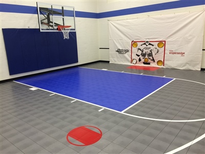 Indoor home basketball court with gray flooring, a blue painted key area, a red shooting circle, a basketball hoop, and blue wall padding.