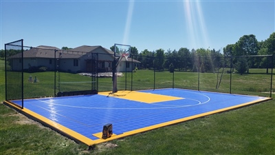 A vibrant backyard basketball court in Medina, MN with high-quality outdoor basketball flooring in blue and yellow, featuring a sturdy hoop and netting, set against a backdrop of a spacious yard and home.