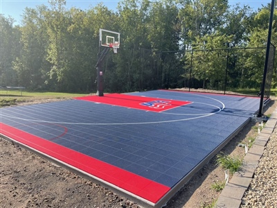 A basketball court with a graphite grey and red surface, featuring white lines and a sport court logo in the center.