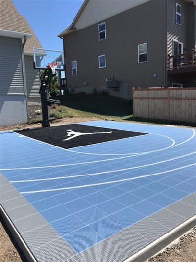 A basketball court with a blue and black surface, grey border, white lines, and a sport court logo in the center.