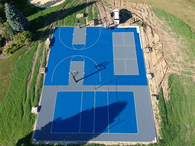 Outdoor residential sports complex with blue and gray surfaces, featuring two basketball courts and two tennis courts, surrounded by grass and trees in Milwaukee.