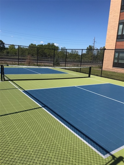 Outdoor sports court with a green and blue surface, white lines, and a black fence.