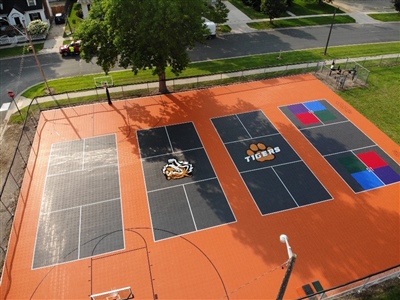 Multipurpose outdoor sport court with orange and black flooring, with tennis courts, hopscotch, and a basketball court.