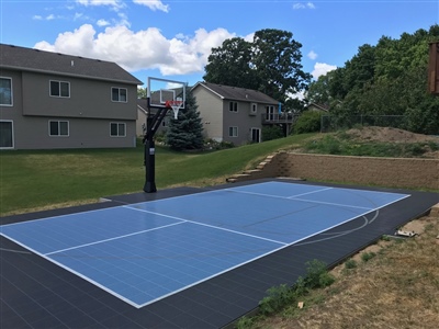 Outdoor residential court with blue and white surface and a black basketball hoop.