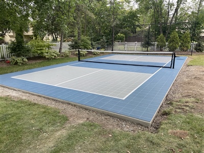 Outdoor residential court with blue and gray surface, featuring a pickleball nets, and surrounded by trees in Wasuau.