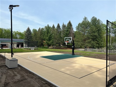  Outdoor residential basketball court with a beige and green surface, and a basketball hoop.