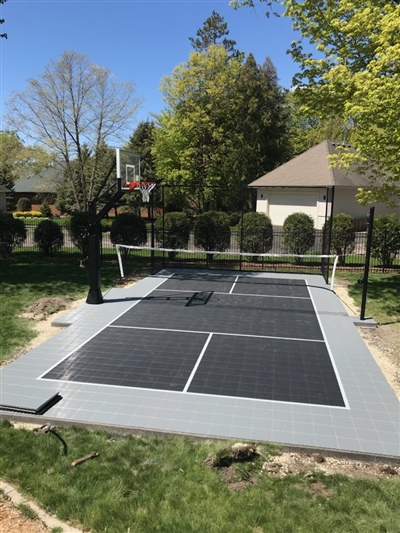 Outdoor residential sports court with a gray and black surface, a basketball hoop, and a tennis net in Green Bay. 