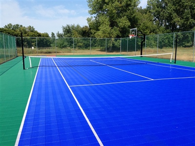 Outdoor sports court with a blue and green surface, featuring tennis nets and a basketball hoop.