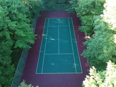 Outdoor tennis court with a green and red surface surrounded by trees in Delafield.