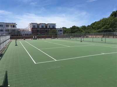  Outdoor sports court with a green surface and white lines, featuring multiple tennis nets, surrounded by a fence.