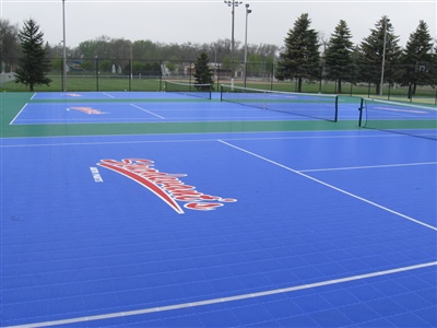 Outdoor sports court with a blue and green surface, multiple logos, and multiple tennis courts.